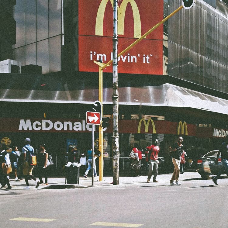 Street scene in town with a McDonald's storefront, pedestrians, traffic lights, signage, and urban movement